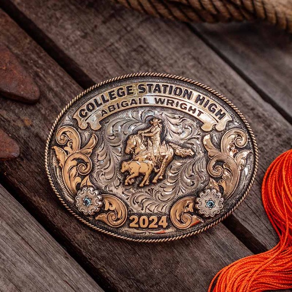 A custom rodeo belt buckle for College Station High with personalized name featuring a team roping rodeo figure, golden scrolls and flowers